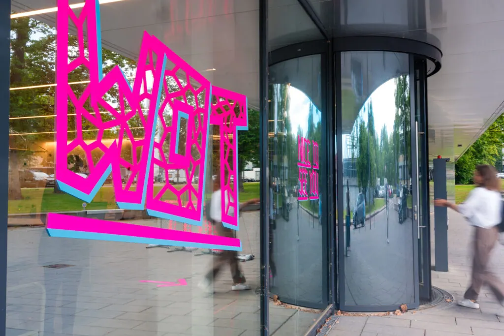 Pinkes Wandbild mit dem Schriftzug WOT an der Glasfassade der Women of Tech Conference 2026