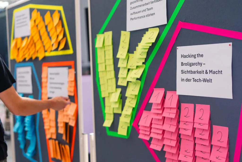 Pinnwände mit bunten Klebezetteln und Themenkarten, etwa „Hacking the Broligarchy“, bei der Women of Tech 2026