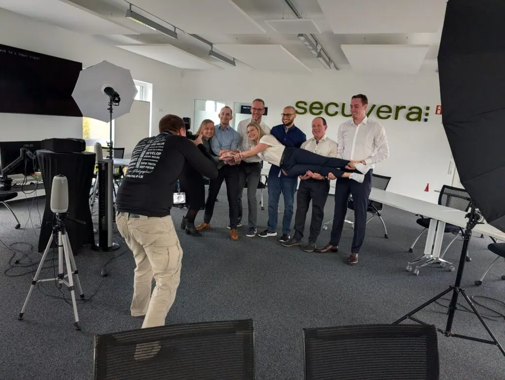 Fotograf fotografiert eine Gruppe von Mitarbeitenden im Besprechungsraum, eine Person wird waagerecht gehalten