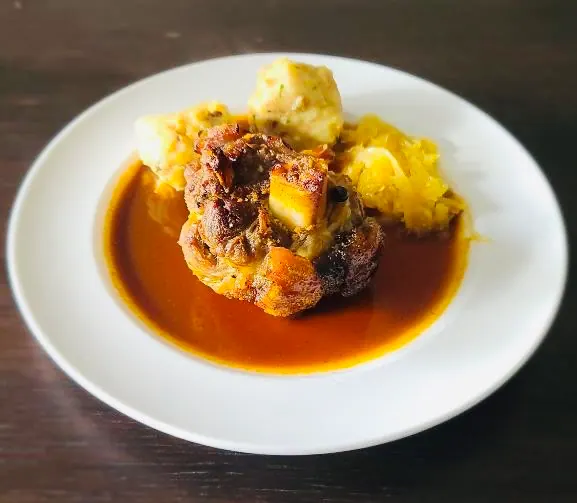 Teller mit Schweinshaxe in Kümmel-Biersauce, Sauerkraut und Semmelknödel vom gemeinsamen Mittagessen beim Teamtag