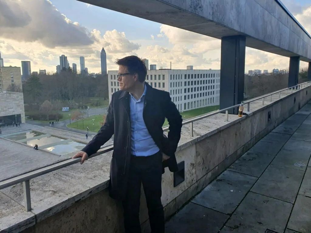 Mann an einer Terrasse der Goethe-Universität Frankfurt mit Blick auf die Hochhäuser der Stadt
