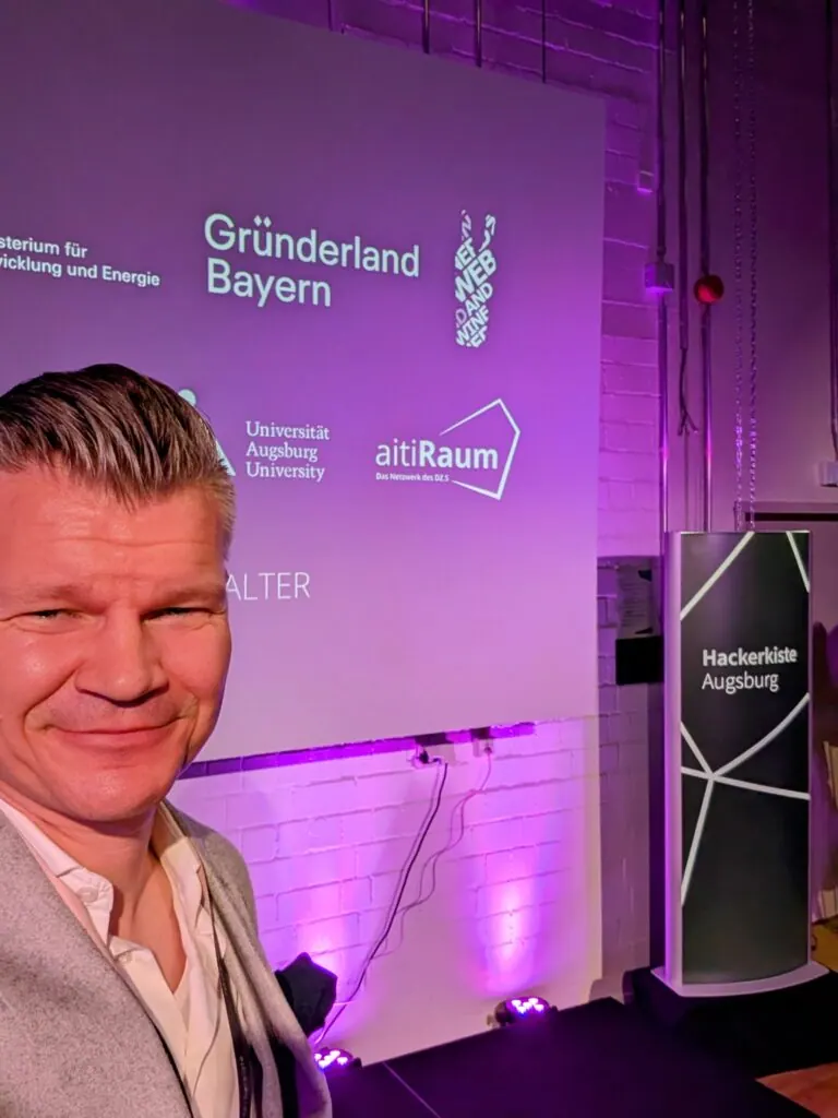 Selfie eines secuvera-Vertreters vor der Leinwand und dem Schild der Hackerkiste Augsburg