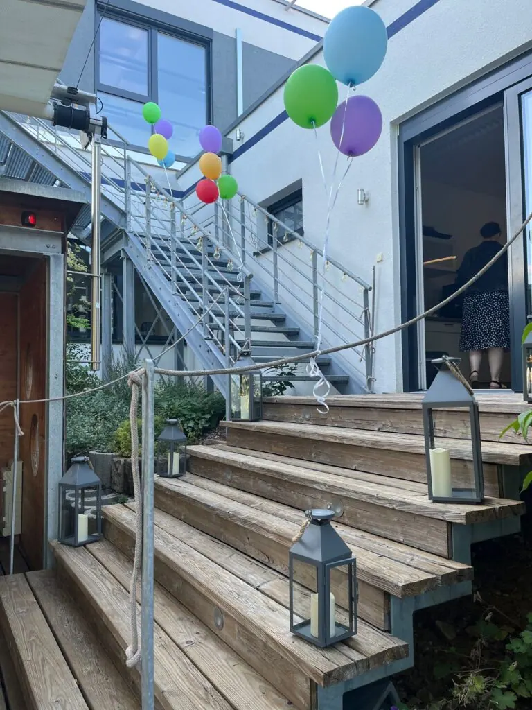 Holztreppe mit Laternen und Seil sowie bunten Luftballons am Gebäude beim Sommerfest 2025