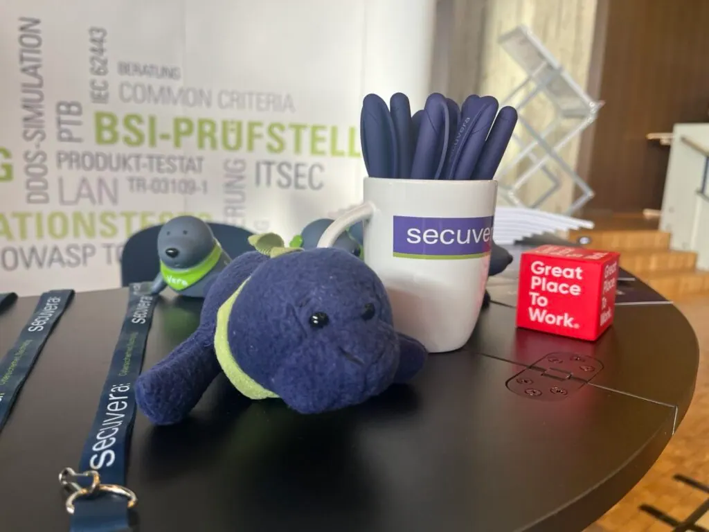 Stand von secuvera mit Maskottchen Vera, Stiftebecher, Lanyards und Great-Place-to-Work-Würfel auf dem Tisch