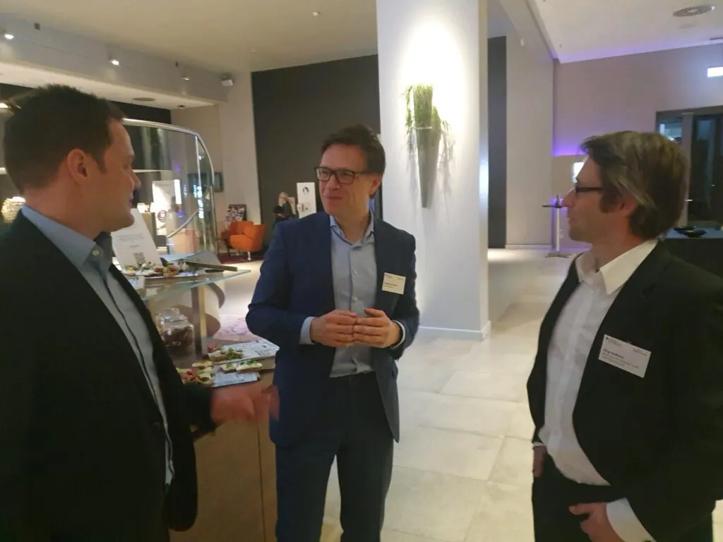 Drei Teilnehmer im Gespräch im Foyer bei der Veranstaltung des BSI-Förderprogramms zu 5G/6G-Sicherheit