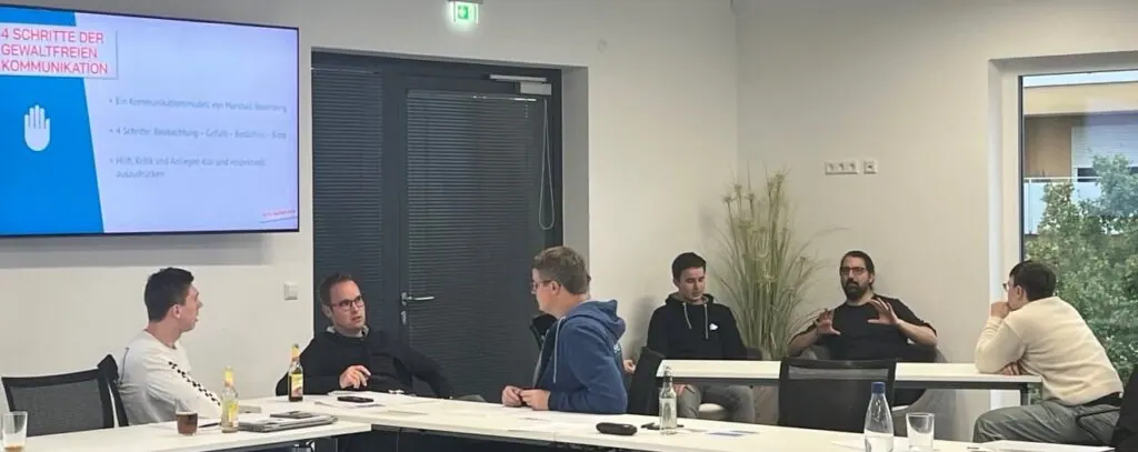 Teilnehmende diskutieren im Seminarraum, links eine Folie zu den 4 Schritten der gewaltfreien Kommunikation