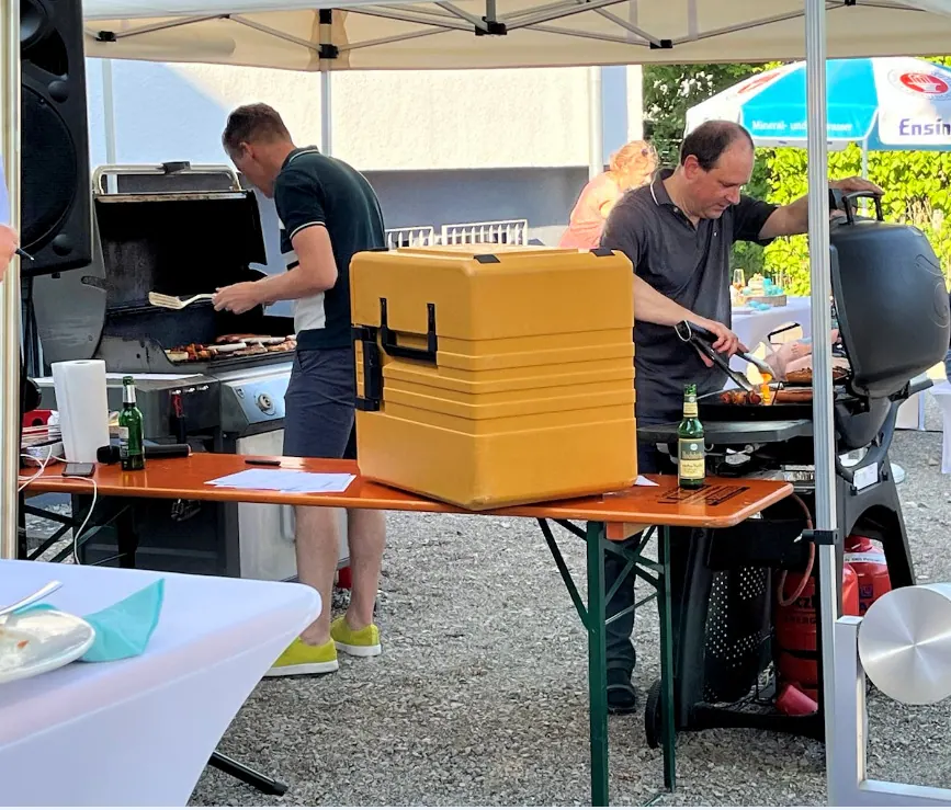 Zwei Männer grillen unter einem Pavillon beim Sommerfest 2022, davor ein gelber Thermobehälter