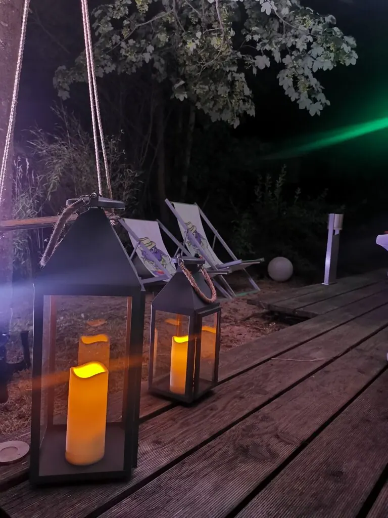 Laternen mit Kerzen auf der Holzterrasse, dahinter Liegestühle, beim Sommerfest 2023 am Abend