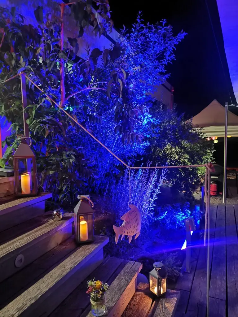 Blau beleuchtete Holztreppe mit Laternen und Blumen beim Sommerfest 2023 am Abend