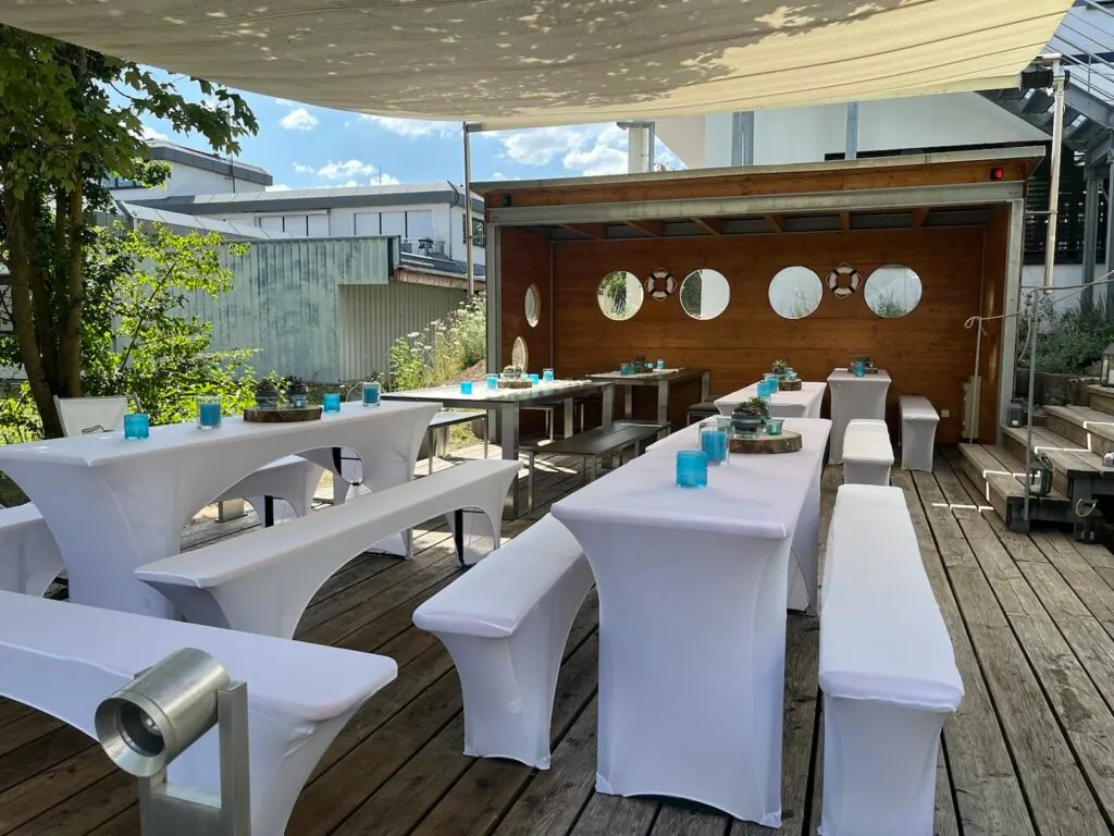 Mit weißen Hussen gedeckte Tische und Bänke auf der überdachten Firmenterrasse beim Sommerfest 2022