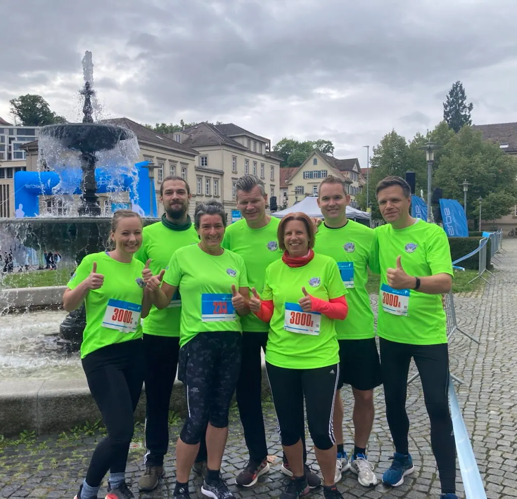 Sechs Läufer:innen von secuvera in neongrünen Laufshirts mit Startnummern vor einem Brunnen in Tübingen
