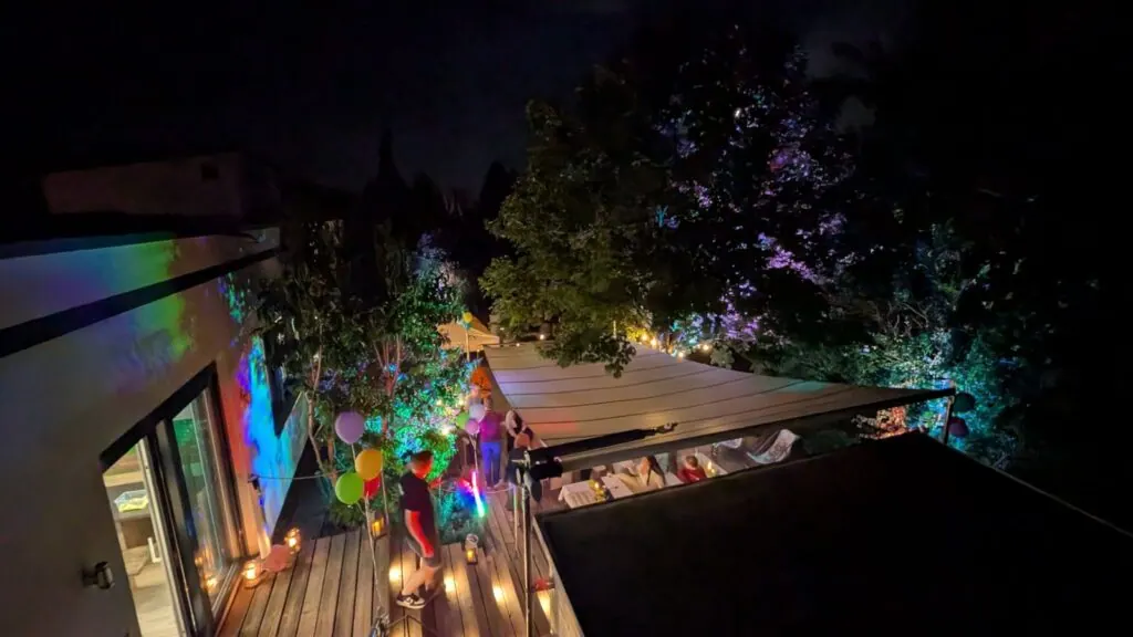 Blick von oben auf die nächtliche Firmenterrasse mit Sonnensegel, Luftballons und Gästen beim Sommerfest 2025