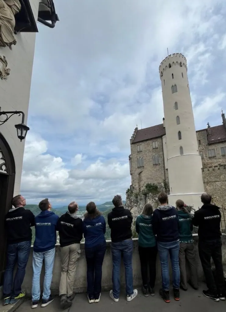 Mitarbeitende in secuvera-Hoodies blicken von hinten am Geländer zur Burg hinauf