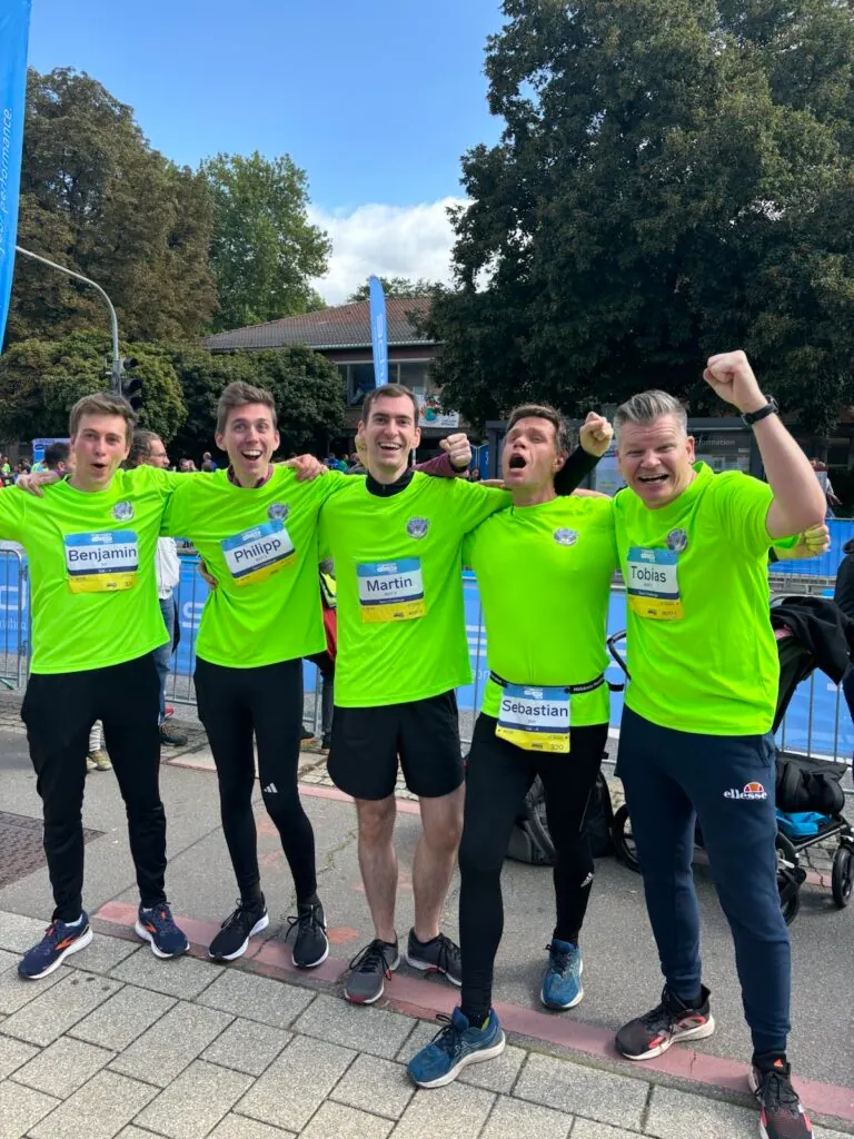 Fünf jubelnde Läufer des secuvera-Teams in neongrünen Shirts mit Startnummern beim Tübinger Erbe-Lauf 2024
