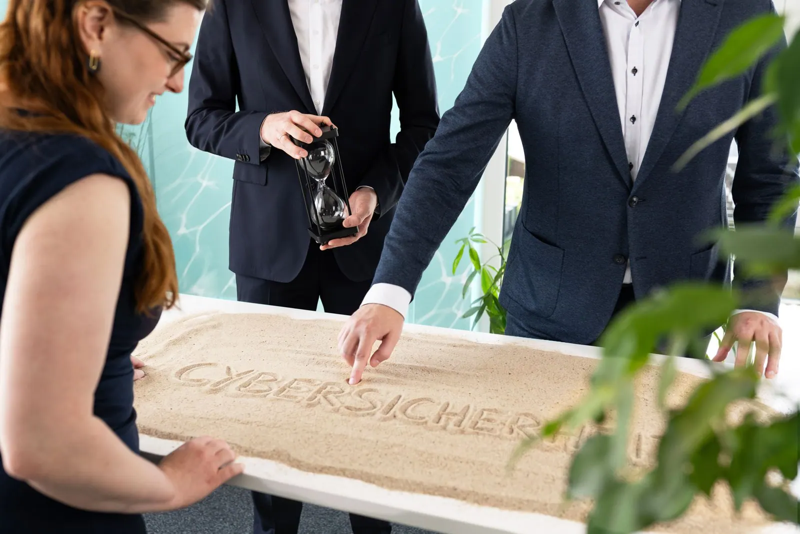 Planspiel am Sandtisch: Eine Person zeigt auf das Wort CYBERSICHERHEIT im Sand, eine andere hält eine Sanduhr