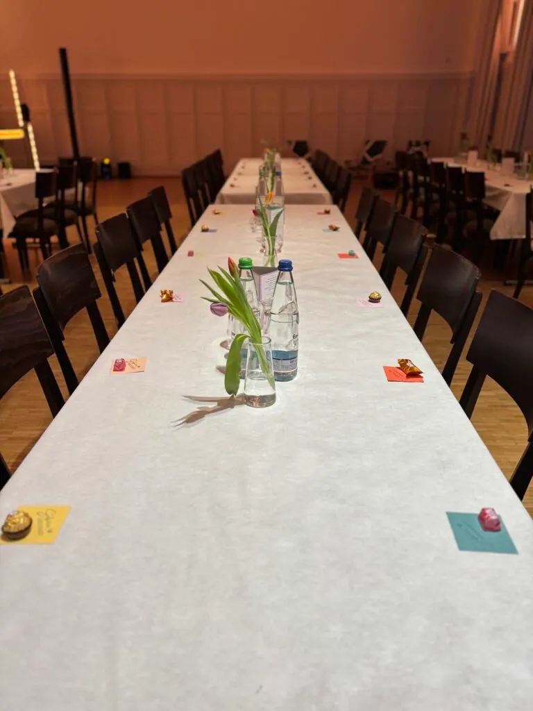 Lange, weiß gedeckte Tafel mit Tulpen, Wasserflaschen und kleinen Süßigkeiten im Festsaal der Jahresfeier