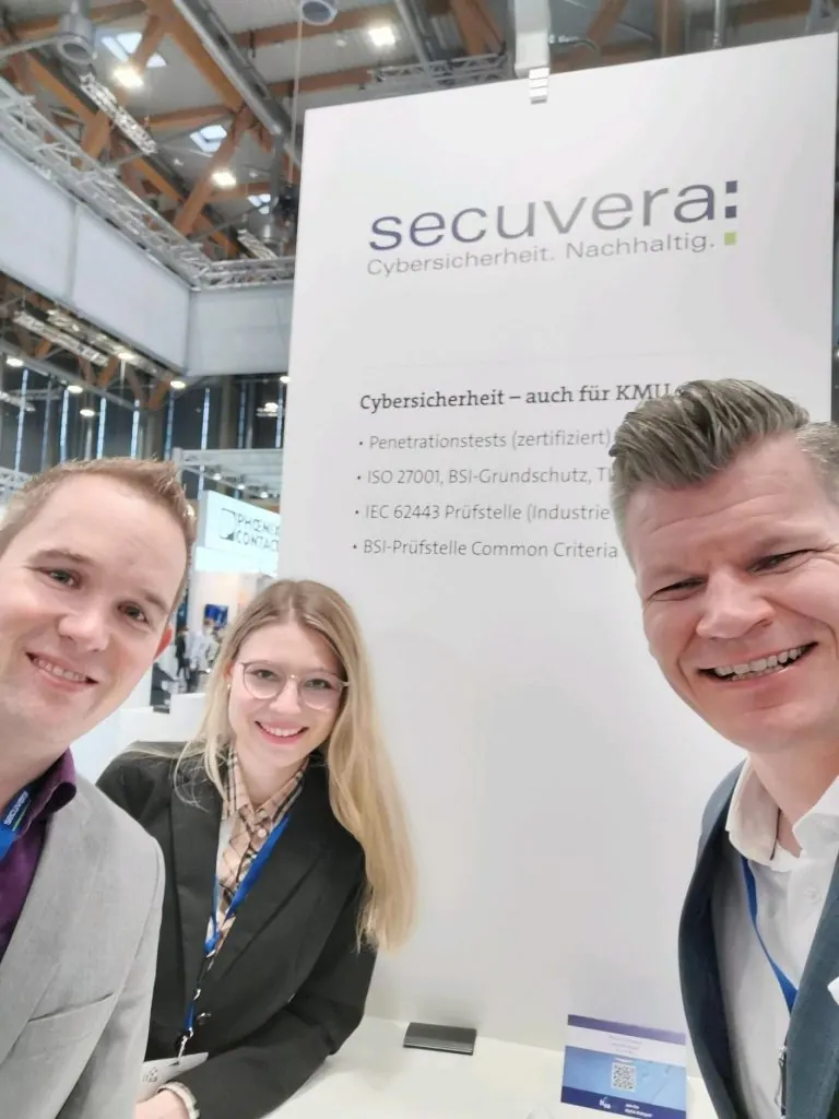 Drei Mitarbeitende von secuvera vor der Stellwand am Messestand der it-sa 2021 in Nürnberg